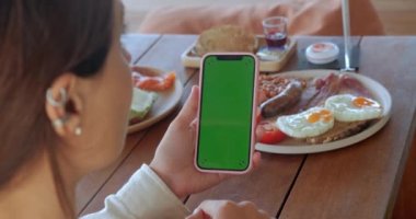Yemekten önce kadınların el ele tutuştuğu yeşil ekranlı cep telefonunu kafenin arka planında kapatın. Restoranın arka planında modern cep telefonunun krom anahtarıyla jest yapan bir kadın..