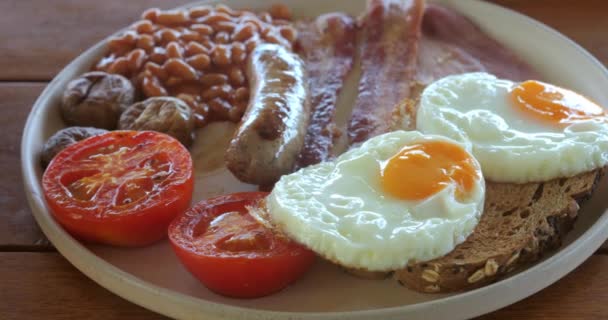 关闭油炸不健康食品 传统的全英式早餐放在木制桌子上的盘子里 英国菜 熏肉和腊肠 不健康早餐概念 — 图库视频影像