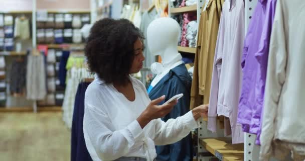 Сознательная Многонациональная Молодая Женщина Осматривает Новую Одежду Магазине Одежды Ищет — стоковое видео