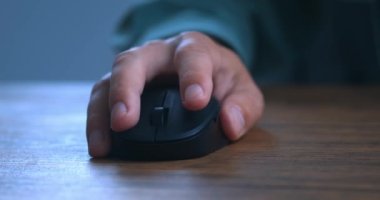 Close-up of a mans hand using a black computer mouse at a wooden table. Closeup male hand scrolling wheel and clicking buttons with computer mouse. The concept of working on laptop computer.