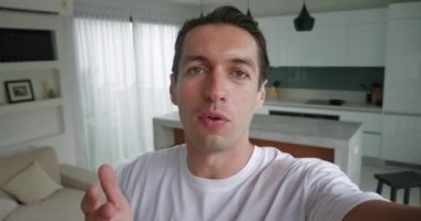 Selfie görüntülü genç adam akıllı telefon tutuyor, evdeki kamerayla konuşuyor. Erkek, modern iç mekânda görüntülü konuşma yapıyor. Blogcu dairesinden görüntülü konuşma yapıyor