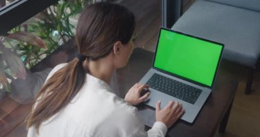 Başarılı bir iş kadını Cafe Table 'da oturuyor ve modern kafede Yeşil Ekran Laptop üzerinde çalışıyor. İşadamı Kadın Krom Anahtar Bilgisayarında Dokunmatik Pad kullanıyor. Omzundan vurulmuş. Dizüstü bilgisayarda çalışıyor