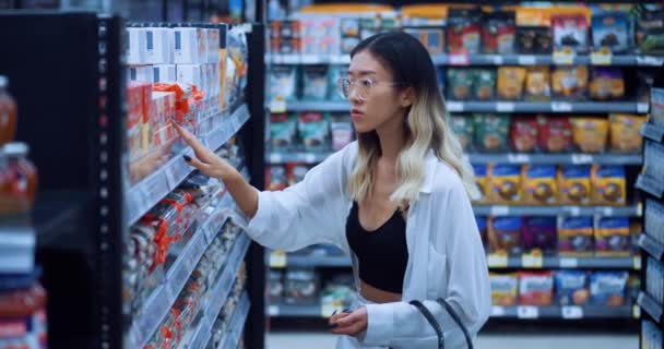 食料品店の女性買い物客の肖像は 食料品店で買い物をしながら 製品は最高の価格を見て選択します 籠を手にした若いアジア人女性は食料品店で食べ物を選ぶ — ストック動画