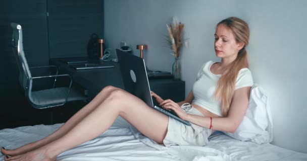 여성은 집에서 편하게 시간을 보내며 침대에 누워서 컴퓨터로 네트워크를 읽습니다 — 비디오