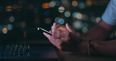 Erkek el bilgisayarda çalışırken gece vakti cep telefonunda geziniyor. Akıllı telefon kullanan, sosyal ağda gezinen biri. Erkek el, cep telefonundaki uygulamadan haber kaynaklarını tara