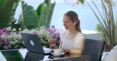 Gülümseyen iş kadını, internette bilgisayarlı video konferans uygulamasında iş arkadaşlarıyla konuşuyor, açık kafede seyahat ederken oturuyor. Dijital göçebe konsepti. Bilgisayardan konuşan bir kadın sanal görüşme görüntüsü.