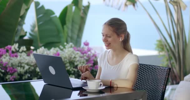 笑顔のビジネス女性は旅行中に屋外カフェに座って ラップトップのオンラインビデオ会議アプリケーション上の同僚に話します デジタルノマドの概念 ラップトップの仮想会議ビデオ通話を話している女性 — ストック動画
