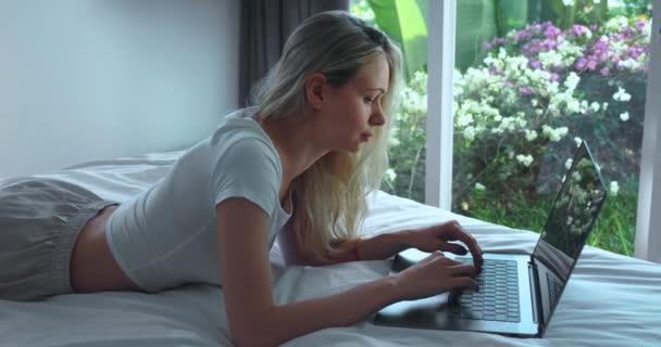 침대에 아름다운 금발의 밀레니엄젊은 침실에서 쉬면서 노트북 컴퓨터를 사용하는 기쁘게 — 비디오