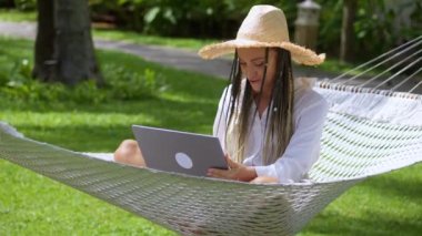 Genç başarılı kadın serbest yazar, yaz tatili sırasında hamakta dinlenirken bilgisayarla piyango kazanan dizüstü bilgisayara bakın. Kadın dizüstü bilgisayara bak zaferi kutla.