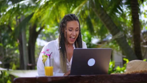 夏休みに屋外のトロピカルカフェに座っているノートパソコンの画面を見て ビジネスの成功率を獲得して喜んで幸せな女性 興奮した女性宝くじ勝者は幸せな成功を喜びます 勝者のコンセプト — ストック動画