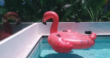 Yaz tatilinin güneşli bir gününde lüks otel otelinde yüzme havuzunda yüzen devasa şişme pembe flamingo oyuncağı. Lüks yaşam tarzı yaz tatili seyahati