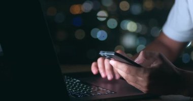 Bilgisayarda touchpad kullanan ve gece geç saatlere kadar çalışırken akıllı telefonunu kaydıran meşgul iş adamını kapatın. Bilgisayarda çalışan adamı kapat ve akıllı telefonu elinde tut..