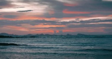 Ufukta dalgalar ve renk bulutlarıyla deniz suyunun üzerinde gün doğumu. Deniz sahili gün doğumu ve renkli gökyüzü bulutları. Pembe Güneş, tropikal sahilde büyük manzaralı bulutların arasından yükseliyor. Güzel tropikal