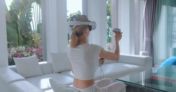 仮想現実デバイスでゲームをプレイする女性 仮想現実ヘッドセットを使用して女性 女性のゲーマーは 自宅でソファに座って アクティブゲームプレイのための仮想現実ヘッドセットとジョイスティックコントローラーを使用しています — ストック動画