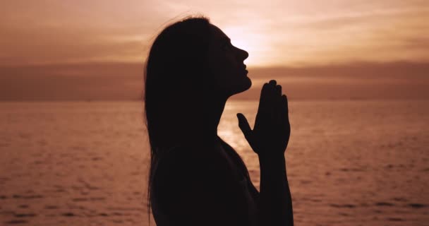 シルエットの若い女性は海の夕日で祈っています 宗教における女性の祈り 真の神への信仰の概念 精神的 希望の概念 神に祈れ — ストック動画