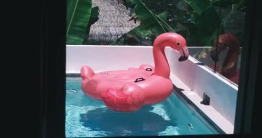 Şişirilebilir pembe flamingo havuz oyuncağı güneşli bir günde özel yüzme havuzunda yüzer. Lüks yaşam tarzı yaz tatili seyahati.