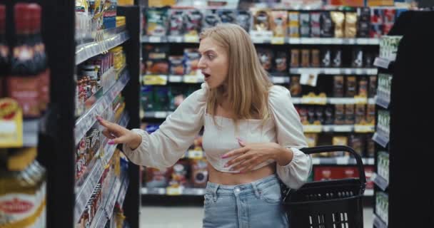高价金发碧眼的女人从货架上查商品 在超级市场上找对了一家杂货店 对价格感到迷惑不解 大眼睛女性立即将产品退回货架上 — 图库视频影像