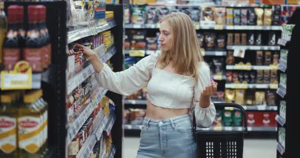 金发碧眼的年轻女性站在超市里检查柜台上的商品 市场上食品杂货店的商品部门的购物或超级市场概念 — 图库视频影像