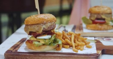 Lezzetli abur cubur konsepti. Izgara sığır burger, eritilmiş peynir ve taze sebzelerle ahşap bir masa ve kızarmış patates kızartması. Sağlıksız abur cubur çok fazla kalori hızlı karbonhidrat.