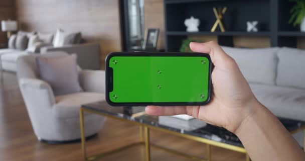 Genç Adam Oturma Odasında Yatay Yeşil Ekranlı Akıllı Telefonu Tutuyor — Stok video
