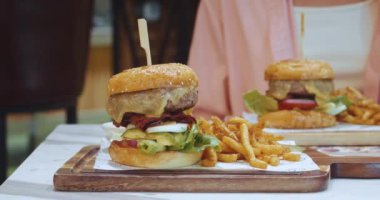 Sağlıksız gıda konsepti. Sığır pirzolası, salatalık ve erimiş peynir ile büyük, lezzetli bir hamburger. Sıcak kafeteryadaki kalorili patates kızartması, sağlıksız beslenmeden kaynaklanan aşırı kiloları hesaplıyor.
