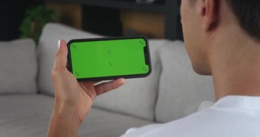 Erkek, evde yeşil ekran maketi olan akıllı telefon kullanıyor, yeşil ekrana vuruyor, cihaz kullanıyor. Omzundan vurulan adam elinde yatay yeşil ekran telefonuyla akıllı telefon tutuyor..