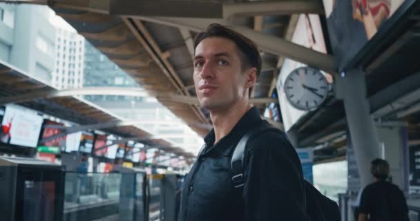 在现代城市中心 千年男性游客带着背包和智能手机站在公交车站等电车 在城市地铁站站台等火车的人 旅行概念 — 图库视频影像