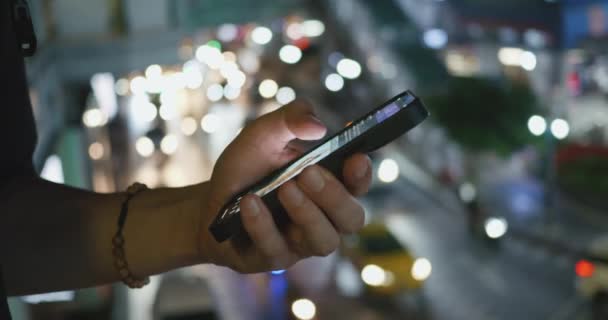 夜の街を背景にスマートフォンのクローズアップ 男性は夜間のバックドロップシティでスマートフォンをスクロールします 自動車を通過する背景にあるスマートフォンを活用した都市コンセプト — ストック動画