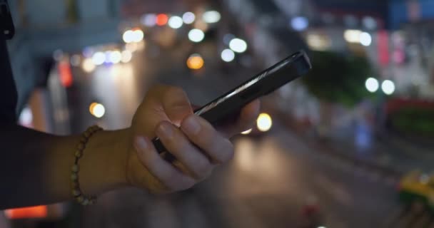 市街地で夜にスマートフォンを使用する人に近づく 男性は彼の携帯電話のアプリでニュースフィードをスクロールします 都市の夜の都市の背景で使用電話で男のシネマティックショット 車を渡る道路 — ストック動画