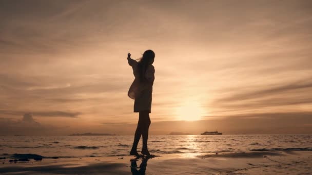 在美丽的金色落日的海滩上 高高地高举着纤细女人的轮廓 快乐的年轻女子在夏日的夕阳西下 感到快乐 自由自在 赤脚在沙滩上跳跃 — 图库视频影像