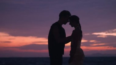 Aşık bir adamın silueti, bir randevu sırasında okyanusta romantik bir akşamın tadını çıkarırken kadınına sarılır. Okyanus kıyısında akşam romantizminin tadını çıkaran aşk eşlerinde. Denizde romantik tatilde kucaklaşan çift.
