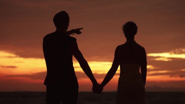 家庭音乐会 在夕阳西下的海面上 恋爱中的男女在黄昏时牵着手 在浪漫的约会中 男人用手指对着女人展示他的梦想 浪漫的家庭梦想 日落时牵着手 — 图库视频影像