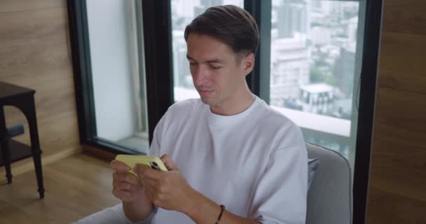 Joven Hombre Millennial Jugando Teléfono Inteligente Sentado Casa Silla Fondo — Vídeos de Stock