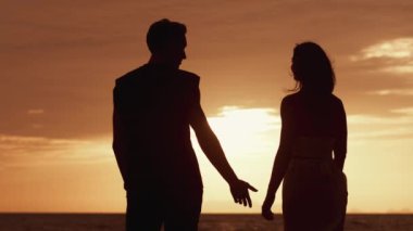 Aşık bir adamın arka görünüşü, bir kadının elini turuncu bir gün batımına götürür. Sevgili bir çiftin gün batımında bir randevu sırasında silueti. Aşkın Kavramı.