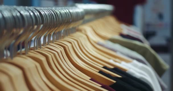 衣架上衣服的概念 市场上一个部门的衣架上的彩色衣服的特写 选择T恤衫 衣服挂在衣架上的商店 基本物品的销售是有利可图的 — 图库视频影像