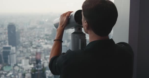 男性观光客通过双筒望远镜观看大城市的摩天大楼 从Mahanakhon塔俯瞰曼谷城市摩天大楼的全景 旅行概念 — 图库视频影像