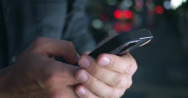 Bir adam tarafından kullanılan akıllı telefonu detaylı bir şekilde çekmek, karanlık çöktükten sonra büyüleyici şehir manzarasına karşı ayarlanmış sosyal medya bağlantısını, mobil interneti ve mesajlaşmayı vurgulamak. Gece vakti akıllı telefon kullanmak.
