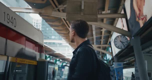 提着背包的男性游客看着一辆路过的火车 等待着他的火车时刻表 千年三十人站在车站等火车 大城市公共交通的概念 — 图库视频影像