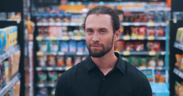 有魅力 留着蓝眼睛 穿着休闲装的大胡子男人站在超市里购物 开心的顾客微笑着在食品超市看相机 — 图库视频影像