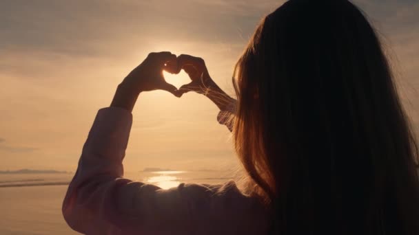 恋爱中的女性旅行者的手在橙色的落日下在海上塑造出了心形 夏季海上旅行时的概念或爱情标志 夏日落日余晖下女性手的心形轮廓 — 图库视频影像