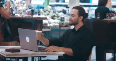 Siyah gömlekli genç sakallı bir adam, bir kafede oturan ve dizüstü bilgisayarında yazan, kahve içen bir site geliştiricisi. Uzmanlaşma web sitesi geliştiricisi. İş veya kişisel kullanım için web sitesi tasarımı oluşturuluyor.