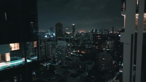 夜の街の近代的な建物の近くで夜間飛行するドローン 夜の空中ドローンビューから街の建物が照らされる 夜のメトロポリスで都市の高層ビルを撮影した映像 アーバン ジャングル — ストック動画