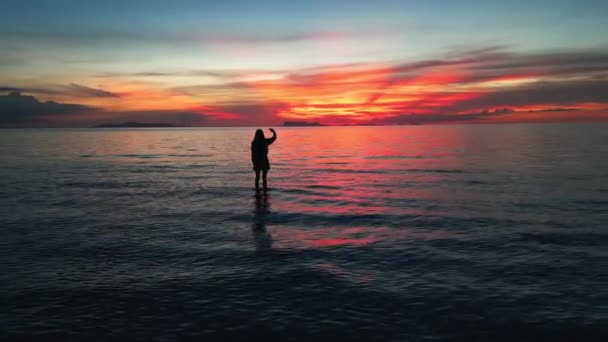 一个女人向地平线外的太阳说再见 挥挥手向逝去的一天告别时的倒影 年轻的女人喜欢海上美丽的落日 — 图库视频影像