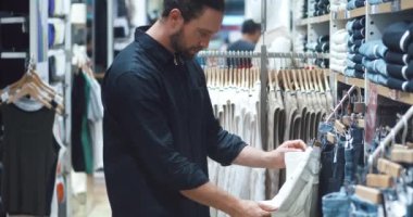 Kapalı giyim mağazasında asılı kot pantolon seçen erkek. Alışveriş merkezindeki kıyafetlere bak. Mağazadaki genç erkek alıcı alışveriş merkezinde yeni pantolon deniyor..