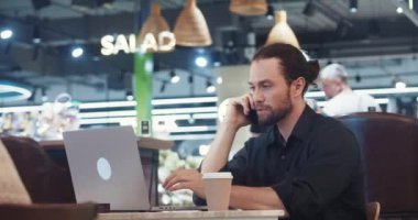 Business Man sosyal medya yöneticisi hesapları yönetiyor ve dizüstü bilgisayarında ilgi çekici içerikler yaratıyor. Sosyal medya yöneticisi çevrimiçi oluyor, dizüstü bilgisayar kullanıyor ve kafede otururken telefona sarılıyor.