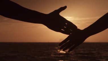 Denizde altın bir günbatımının arka planına karşı bir erkek ve bir kadının el sıkışması silueti. Erkek ve kadın anlaşma konsepti. Mükemmel bir anlaşmanın işareti olarak bir erkekle bir kadının el sıkışması.