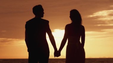 Gün batımında birbirine aşık bir çiftin silueti. Adam kadınına eliyle dokunuyor. Aile gün batımında denizde. Bir çift erkek, bir kadın güneşin önünde ellerini tutuyor. Aşk konsepti.
