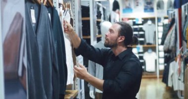Alışveriş, moda, stil insanları, alışveriş merkezinde ya da giyim mağazasında kıyafet seçen takım elbiseli zarif genç adam kavramı. Mağazadaki adam elbise askısına bakıyor. Elbise mağazasında askıda asılı tişört seçerken..