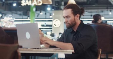 Sakallı adam alışveriş merkezinde oturuyor ve dizüstü bilgisayarda çalışıyor. Erkek yönetici dizüstü bilgisayarında içerik yaratıyor. İçerik oluşturan yeni alan yöneticisi geliştiriliyor.