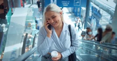 Yürüyen merdivendeki kadın telefonla konuşuyor. Seyahat eden iş kadını yürüyen merdivenden iniyor. İş gezisine gidiyor. Profesyonel şirket yöneticisi, modern yapı ofisi ya da havaalanı